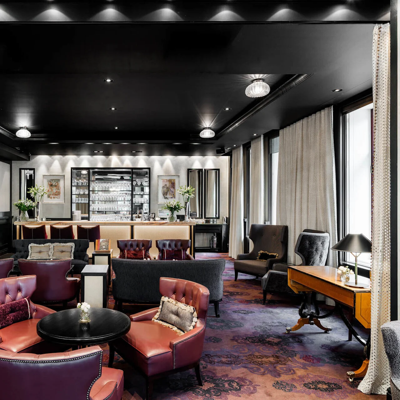 A luxurious lounge features leather chairs and a central bar adorned with flowers, under ambient lighting. Text reads "Kämp 1887," set against elegantly decorated walls with framed art.