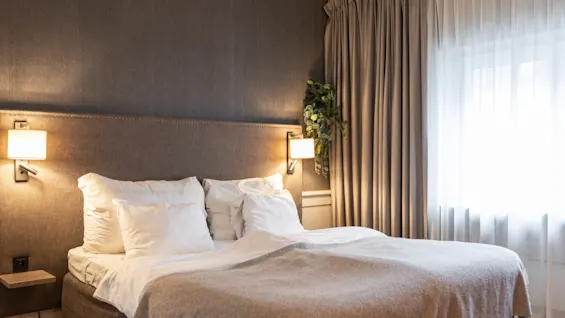 A comfortable and inviting hotel room at Home Hotel Grand Bodø, featuring a neatly made bed, warm lighting, and soft curtains.