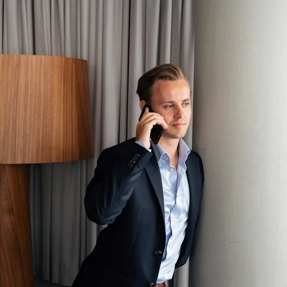 En person i kostym som lutar sig mot en pelare och pratar i mobiltelefon