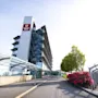 Et høyhus med et "Clarion Hotel"-skilt står i et moderne, beplantet område med grøntområder og blomster, ved siden av en glassgang under en klar himmel.