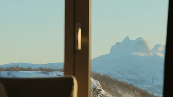 Et fredfyldt vinterlandskab med bjerge set gennem et vindue, med snedækkede tinder og en klar himmel.