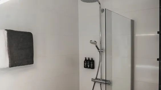 Et moderne badeværelse med bruseområde med hvide flisevægge, et regnbruserhoved, en håndbruser og vægmonterede toiletartikler.