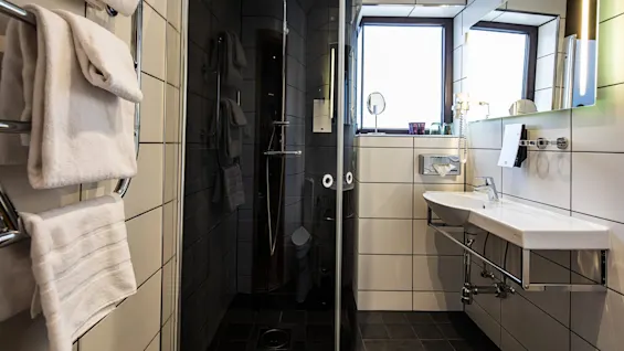 A modern bathroom with a glass shower, white basin, towels, and a mirror against black tiled walls.