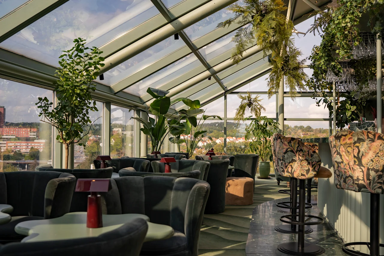 Tyylikäs kattolounge lasikatolla, rehevällä kasvillisuudella ja mukavilla istuimilla, tarjoten panoraamanäkymät kaupunkiin.