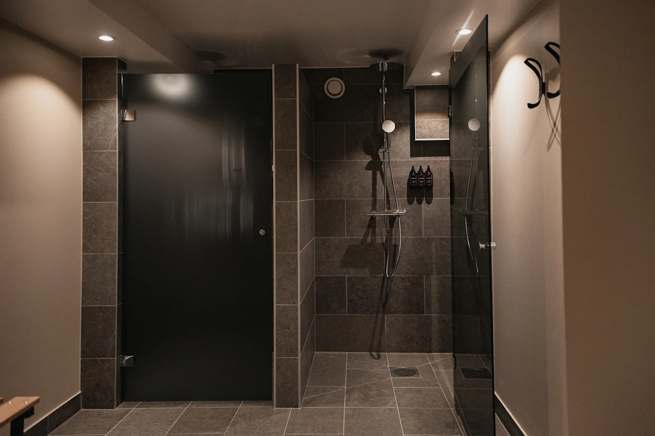 Et moderne og elegant dusjområde med mørke flislagte vegger og gulv, med en glassvegg og en mørk personverndør.