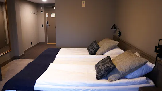 A neatly made bed with pillows in a tidy hotel room with subdued lighting.