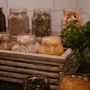 A cozy breakfast spread featuring various cereals, grains, and dried fruits in glass jars, neatly arranged in a rustic wooden tray.
