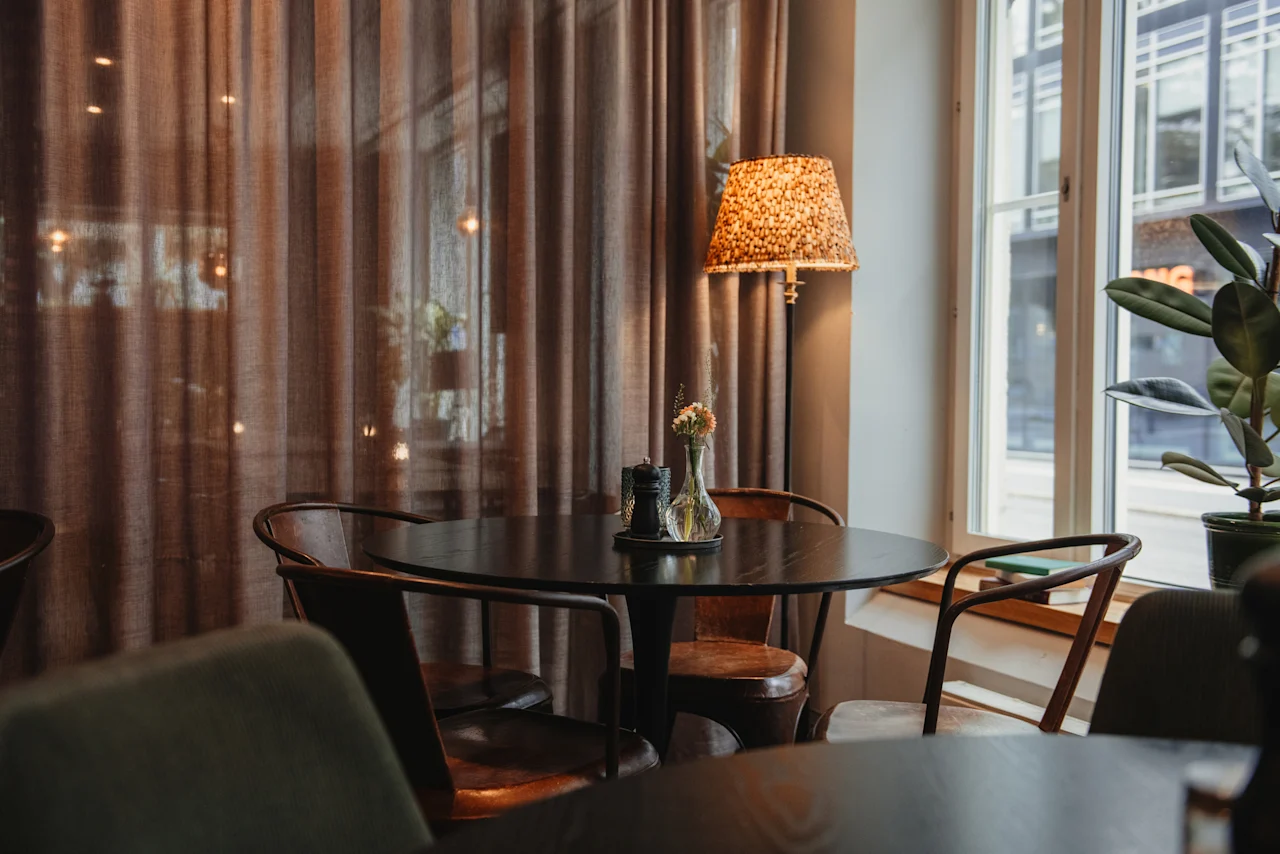 A cozy corner at Home Hotel Uppsala with a round table, chairs, and a floor lamp, bathed in soft light from a nearby window.