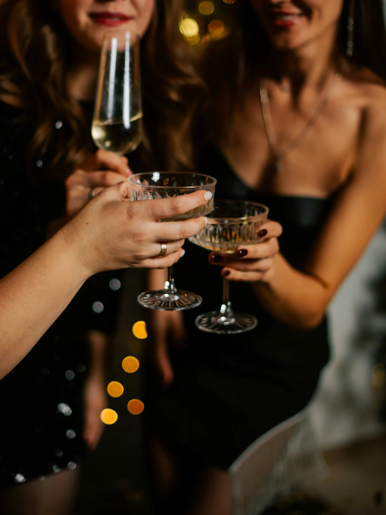 Three people hold glasses in a toast, celebrating in an elegant, warmly lit environment with sparkling lights in the background.