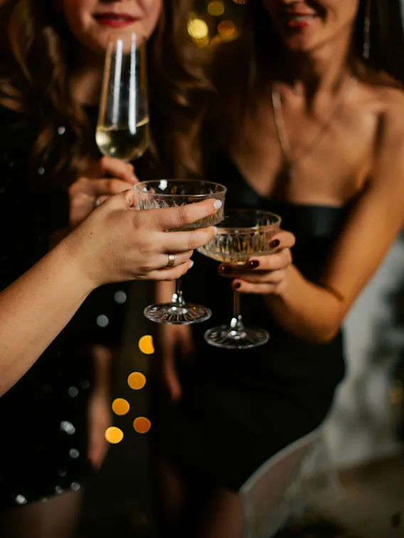 Tre personer håller glas i en skål, firar i en elegant, varmt upplyst miljö med gnistrande ljus i bakgrunden.