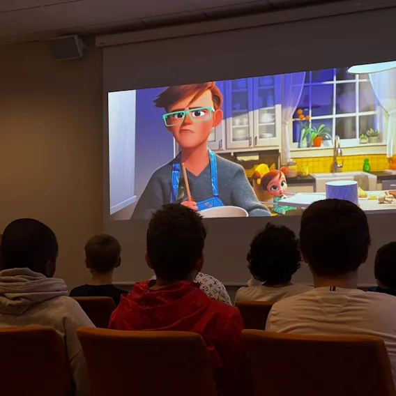 Barn sett bakfra mens de ser på en animasjonsfilm på et stort projiseringsskjerm i et kinorom.