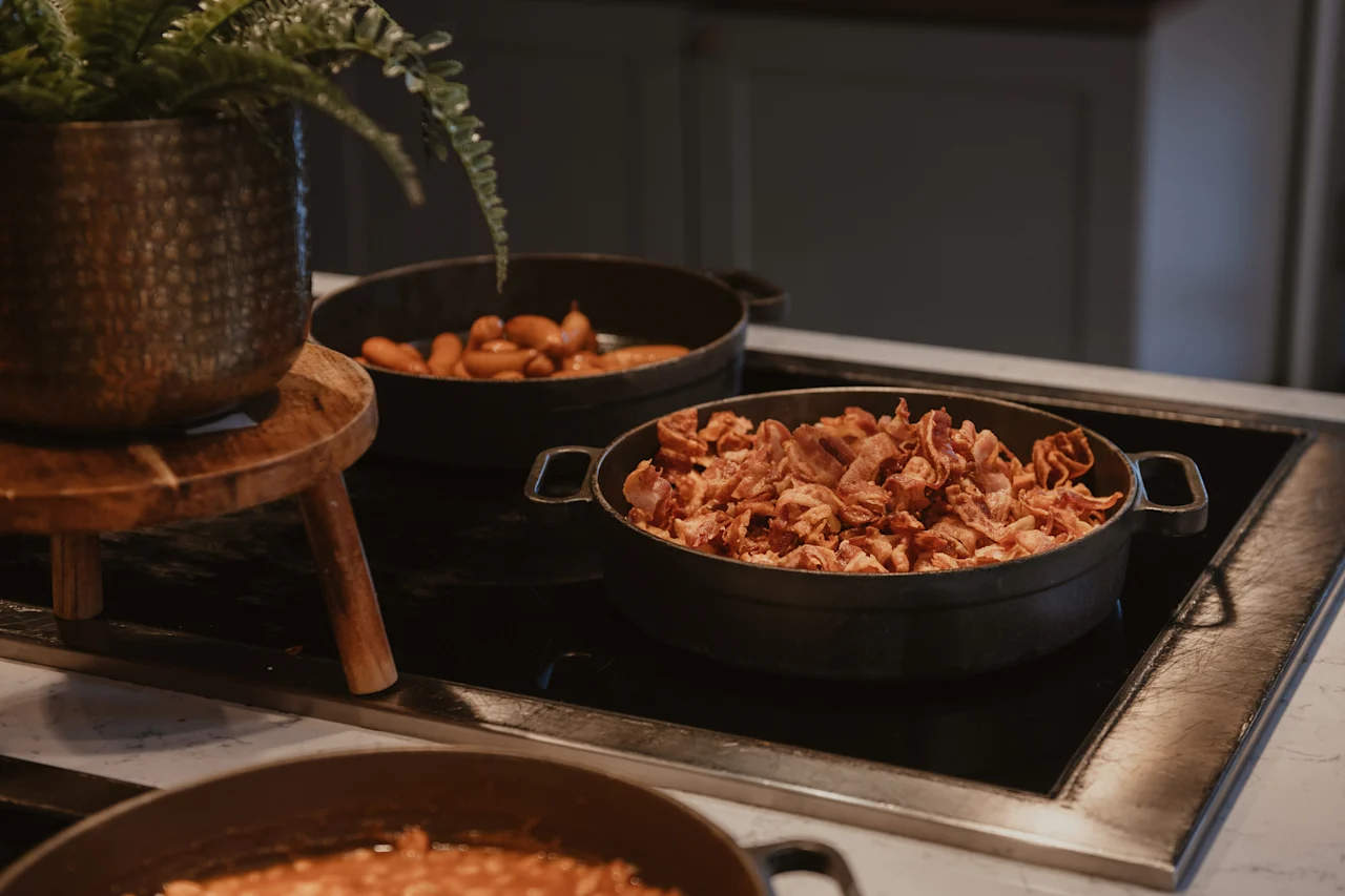 Et nærbilde av en frokostbuffé med sprøtt bacon, pølser og en plante i en dekorativ potte.