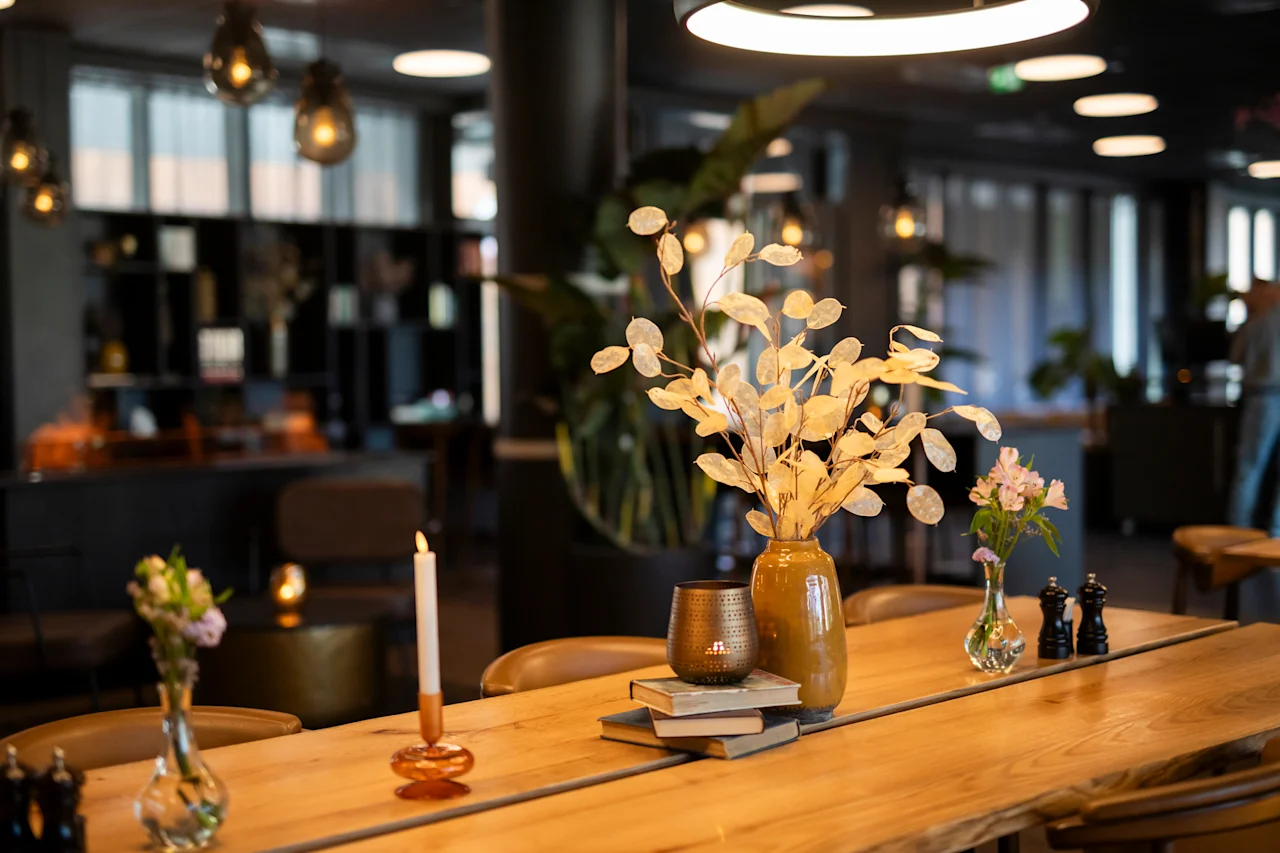 Et koselig spisebord med tørkede blader, rosa blomster, et tent lys og bøker i en dempet restaurant.