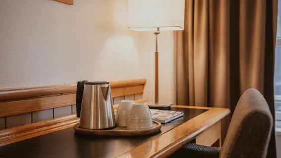 A cozy hotel room desk with a kettle, cups, and a warm lamp, perfect for a relaxing break.
