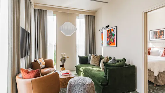 Et stilfuldt hotelsuite-opholdsrum på Hernö Gin Hotel, med en komfortabel grøn sofa, lænestole og et tilstødende soveværelse.
