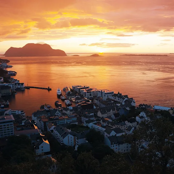 Panoramautsikt over kystbyen Ålesund og fjordene bader i et varmt, gyllent solnedgangslys.