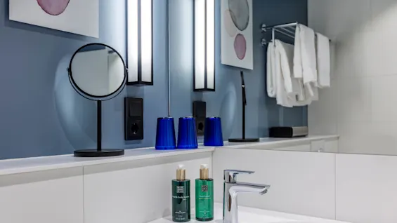 A clean bathroom counter with toiletries, reflecting mirror and wall art; organized and modern.