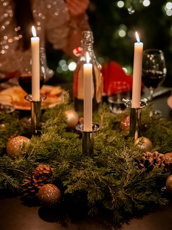 Människor som njuter av en festlig julmiddag runt ett bord dekorerat med ljus och en grön krans.