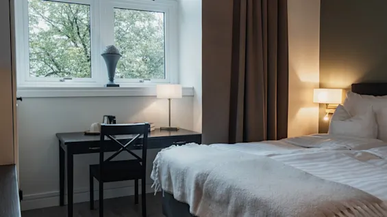 Et koselig hotellrom på Home Hotel Norre Park i Halmstad med en seng, et skrivebord ved et vindu og varm belysning.
