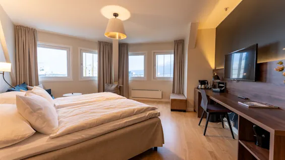 An inviting hotel room with a comfortable bed, a functional desk area, and bright windows offering a pleasant view.