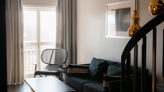 En hyggelig og moderne stue med en mørk sofa, en stilfuld stol og et sofabord. Sollys strømmer ind gennem vinduet.