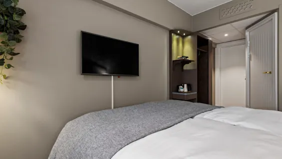 A cozy hotel room with a comfortable bed, a wall-mounted television, and a small refreshment station.