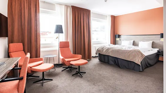 Ett välbelysat hotellrum med säng, sittplats och stora fönster.