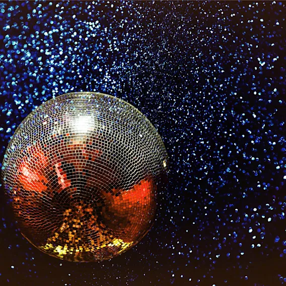 En glitrende discokule reflekterer varmt lys mot en mørk bakgrunn med glitrende blått glitter.