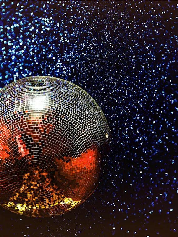 En skimrande discokula reflekterar varmt ljus mot en mörk bakgrund med glittrande blått glitter.