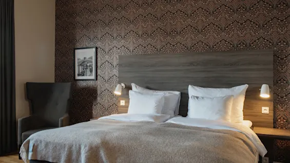 Ett välkomnande hotellrum på Home Hotel Grand, Helsingborg, med bekväm säng, varm belysning och mönstrad tapet.