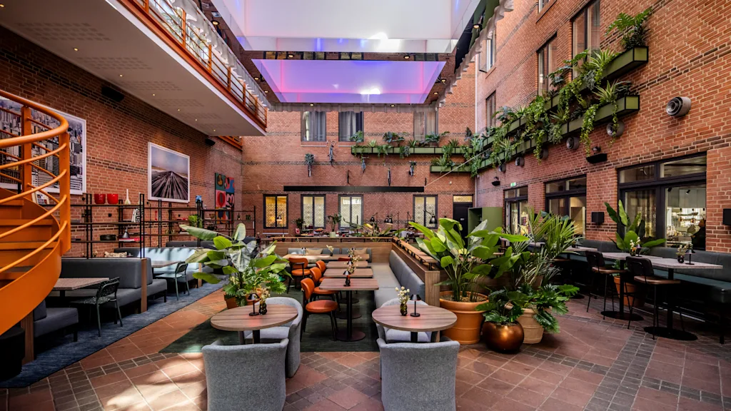 An inviting indoor courtyard at Comfort Hotel Vesterbro with dining tables, lush plants, and brick walls under a bright skylight.