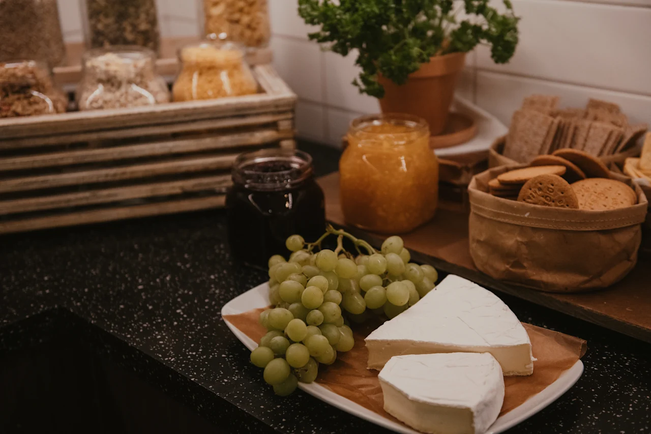 A delightful self-service food station with cheese, green grapes, fruit jams, and various crackers, ready for enjoyment.