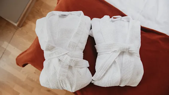 To friske hvide badekåber foldet på en seng, klar til gæster på Home Hotel Wellington.