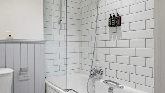 A well-lit bathroom with a white tiled shower and bathtub, alongside a toilet. Wall-mounted dispensers offer convenient toiletries.