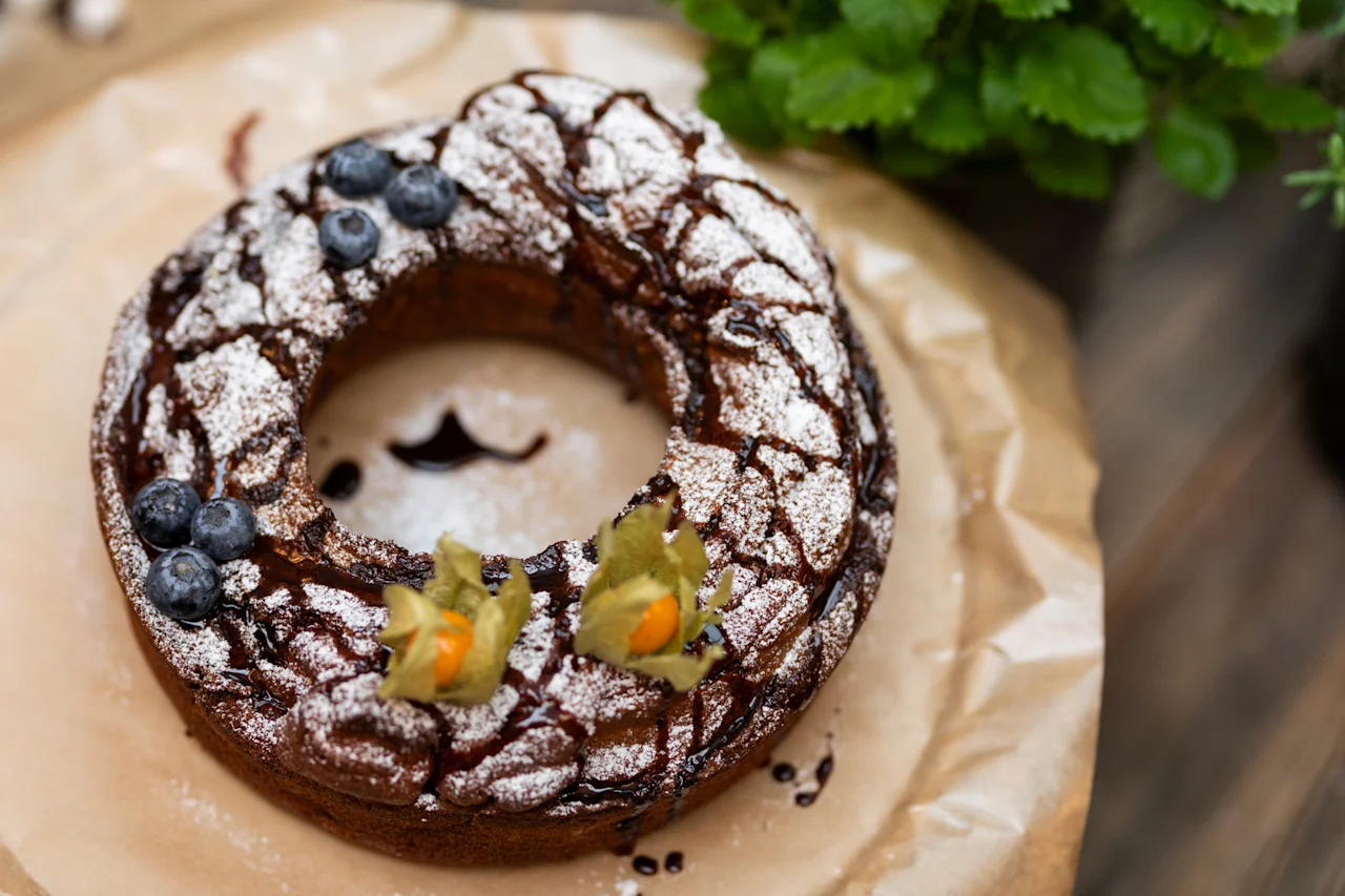 A delicious ring-shaped cake, dusted with powdered sugar and drizzled with chocolate, garnished with blueberries and physalis. Home Hotel Grand Bodø.
