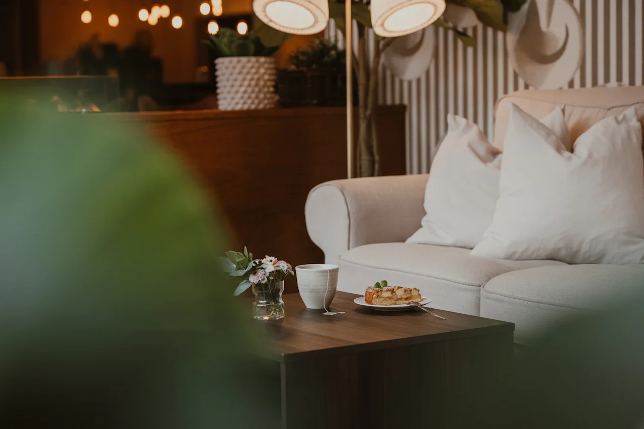 A warm and inviting lounge area with a sofa, a coffee table featuring tea, a slice of cake, and a small bouquet.