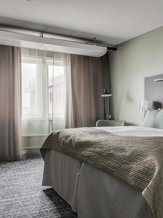 Ett modernt hotellrum med en bekväm säng, ett skrivbord och ett fönster med gardiner, som erbjuder en avkopplande vistelse.