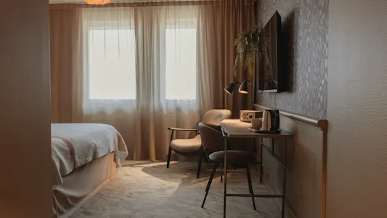 A cozy hotel room with a comfortable bed, a functional workspace, and warm lighting, perfect for relaxation or productivity.