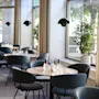 Round tables with chairs are neatly arranged in a modern dining area, featuring large windows and potted plants, creating a bright and inviting ambiance.