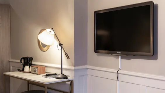 A cozy corner in a hotel room at Home Hotel Grand Bodø with a desk, lamp, kettle, and a wall-mounted TV for relaxation.
