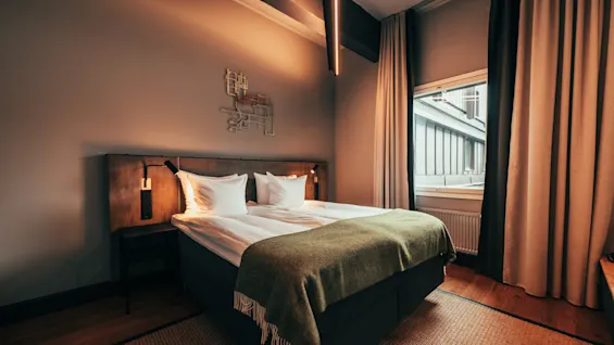 A cozy hotel room with a comfortable bed, warm lighting, and a window with curtains.