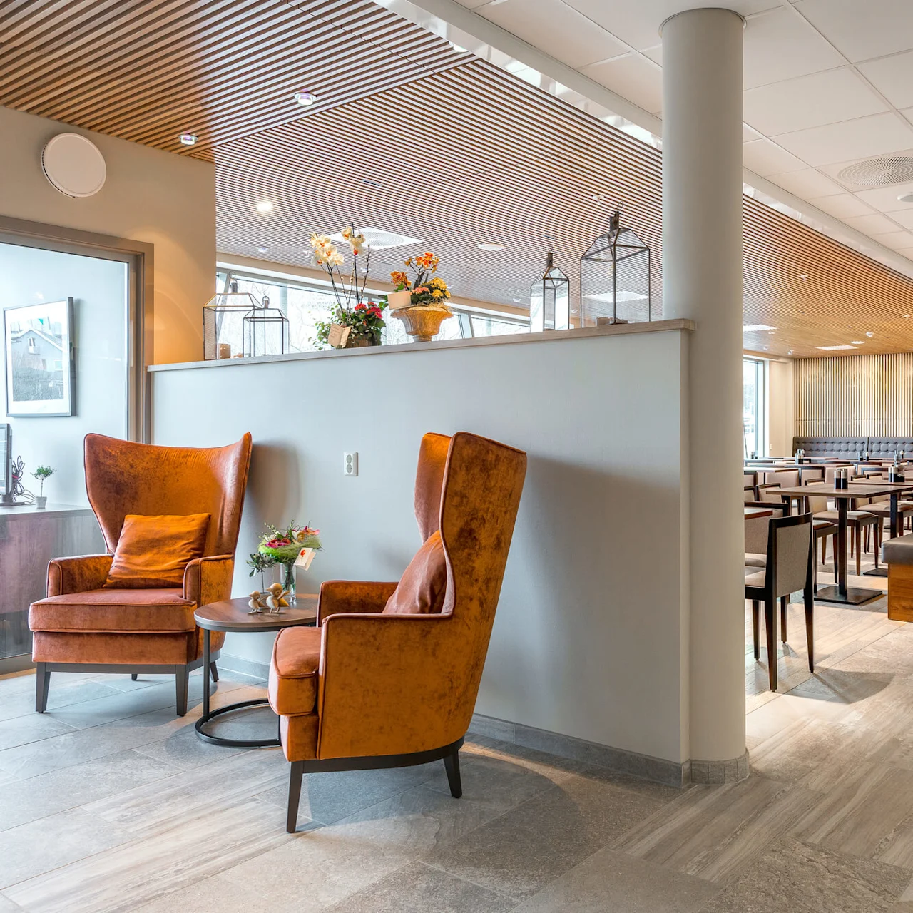 Kaksi mukavaa tuolia sijaitsee modernissa, tilavassa ruokailutilassa, jossa on pöytiä, pehmeä valaistus yläpuolella ja buffet-osio taustalla.