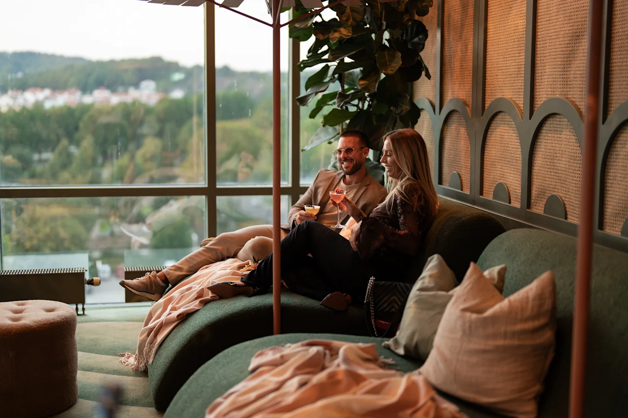 Ihmiset nauttivat cocktaileista ja keskustelusta mukavalla sohvalla modernissa loungessa, josta on luonnonkaunis näkymä ulos.