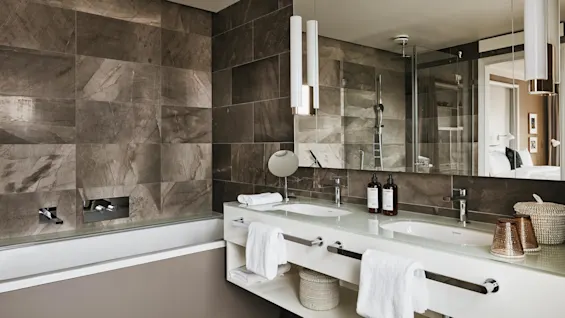 Et moderne bad med dobbelt servant, flasker og håndklær mot et stort speil. De omkringliggende marmorklare forbedrer den elegante, rene estetikken.