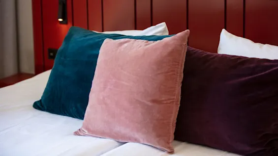 Three decorative pillows on a bed, with a red headboard and a soft light above.