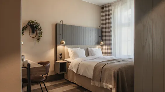 A cozy hotel room with a comfortable bed, a small desk, and a window with curtains, creating a relaxing atmosphere.