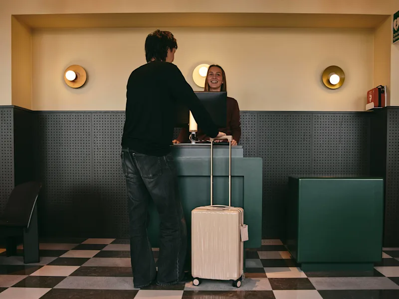 En person med kuffert tjekker ind ved en hotelreception, mødt af en smilende receptionist.