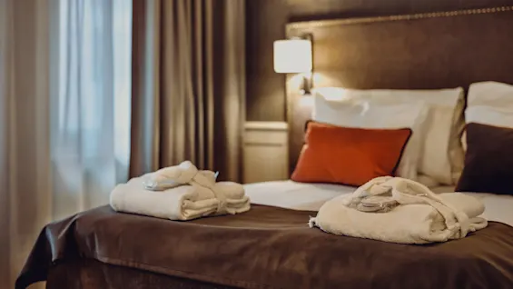 A hotel room with a neatly made bed, decorative pillows, and towels folded in the shape of swans.