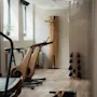 A bright fitness room at Home Hotel Uppsala with modern wooden exercise equipment, including a treadmill, bikes, and weights.