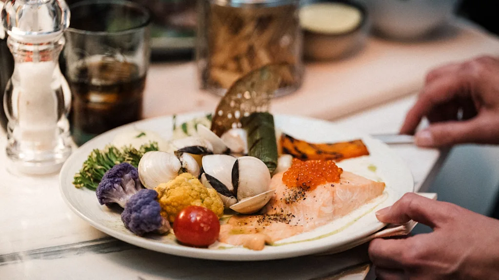 Hender som presenterer et vakkert anrettet måltid med laks, rogn, muslinger og fargerike grønnsaker.